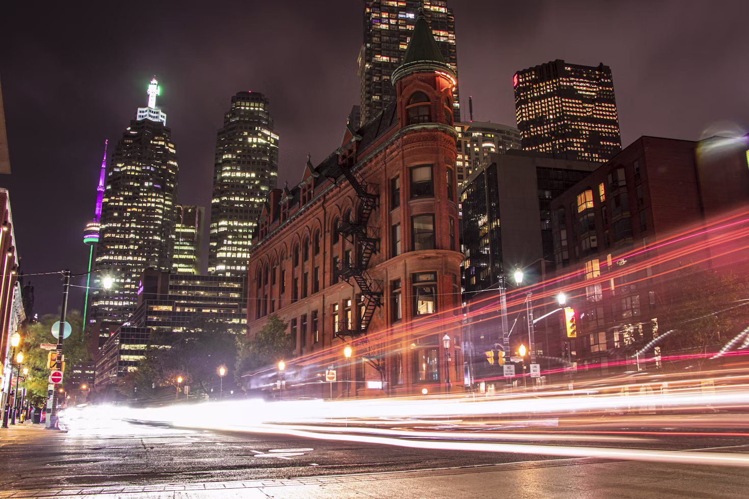 A long-exposure night shot of Front Street in Toronto, with light trails from passing traffic and the CN Tower visible in the distance.